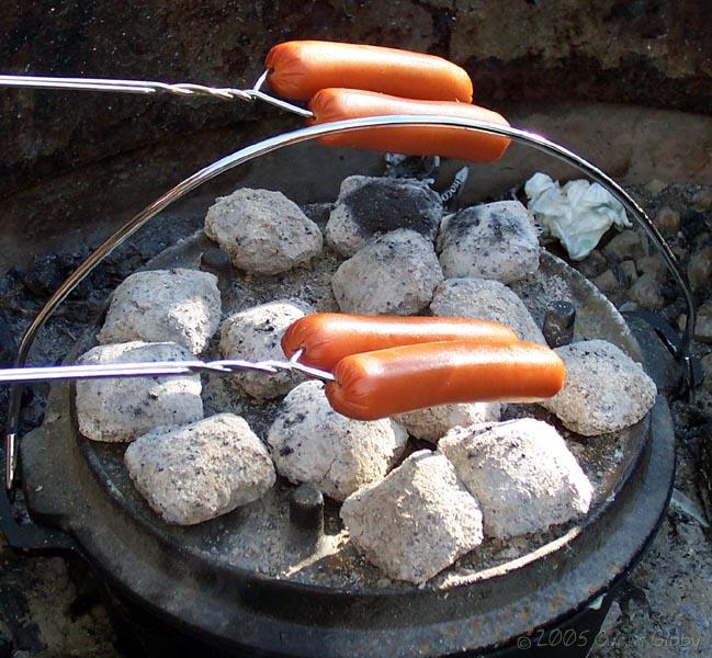 The hot dogs cook over the coals on the dutch oven